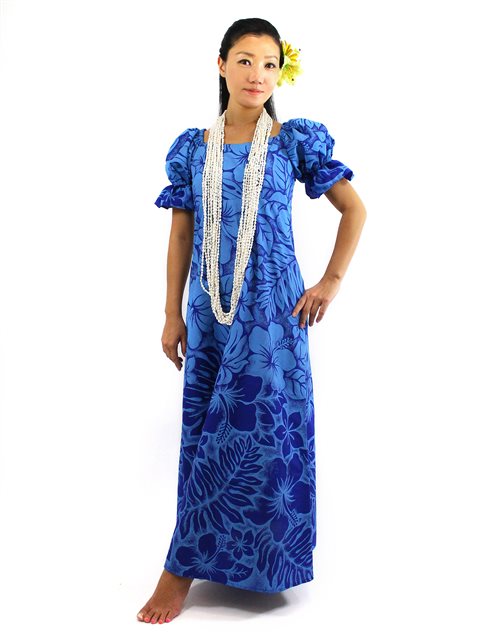 A woman wearing a blue long dress with a floral pattern, featuring frill sleeves and a zipper on the back, accessorized with a white lei and a flower in the hair.