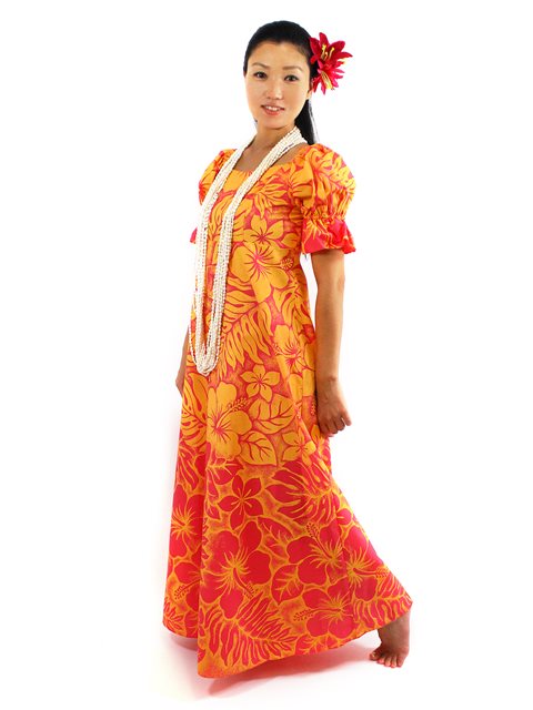 A woman wearing an orange and yellow floral long muumuu dress with a white belt and a red flower in her hair, standing against a white background.