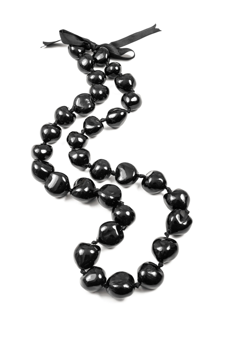 A black kukui nut lei laid out on a plain background, showing glossy-black nuts and a ribbon tie at one end.