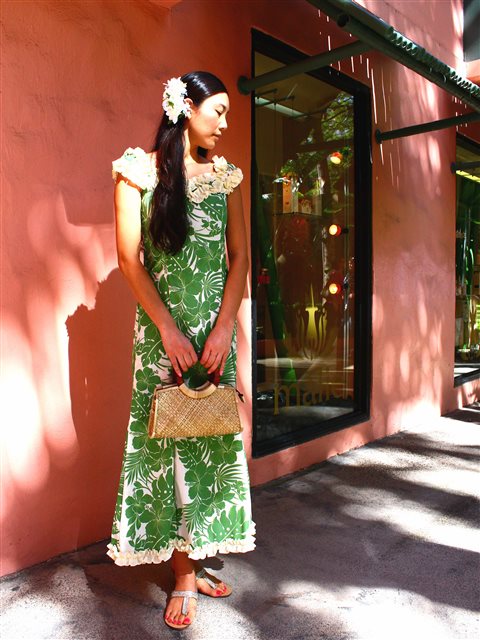 Woman in a green floral dress standing against a pink wall.