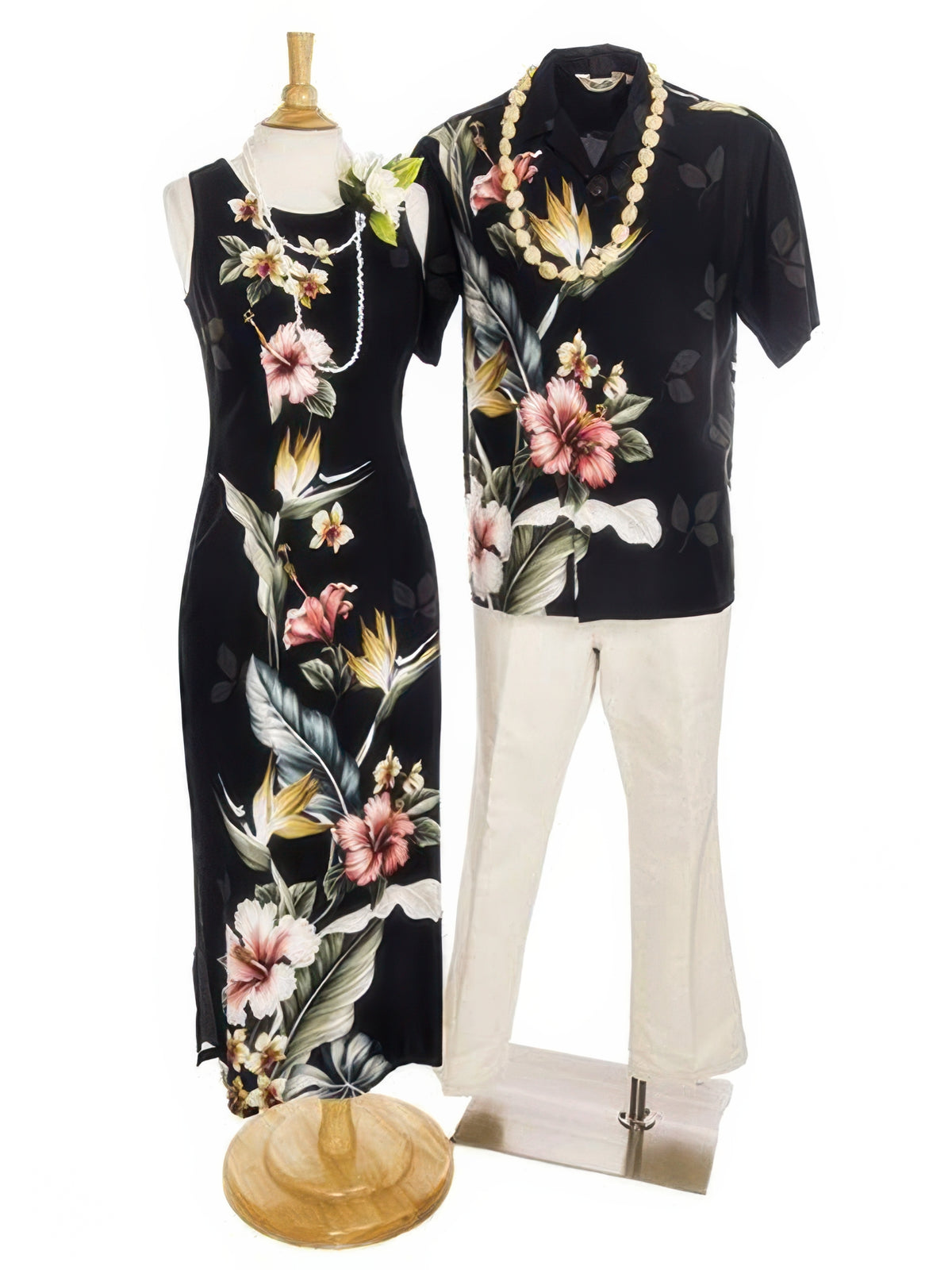 A matching couple's outfit displayed on mannequins against a white background. The set includes a sleeveless black maxi dress with a pink and green floral print on the dress form, and a matching short-sleeve button-up shirt on the standing mannequin, styled with a gold beaded necklace and cream pants.